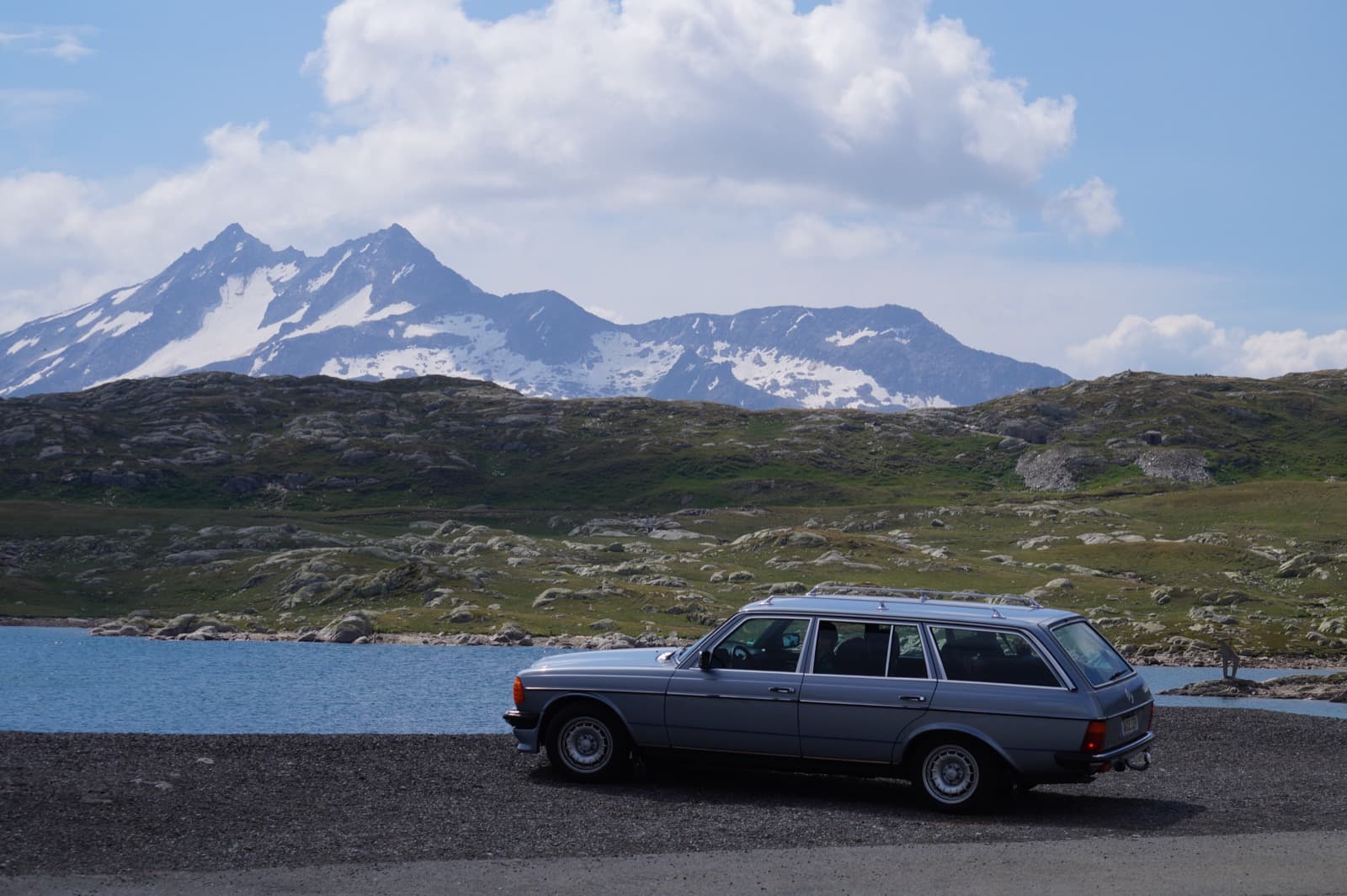 W123 T-Modell an einem Bergsee mit schneebedeckten Gipfeln