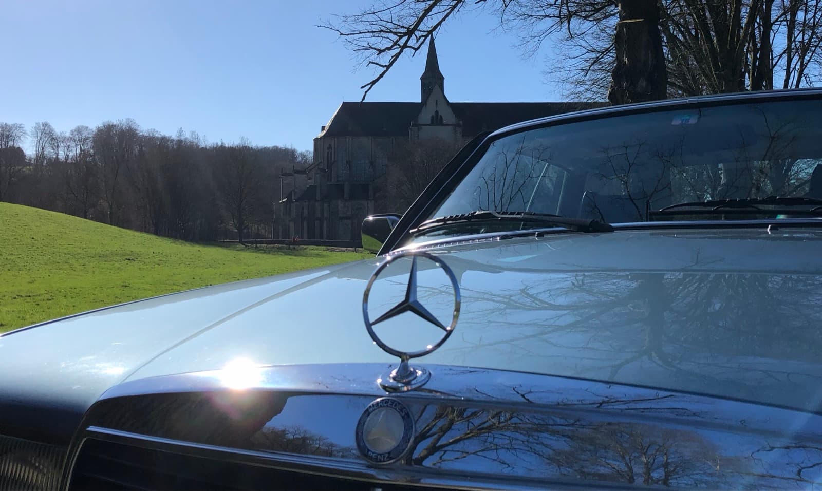 Mercedes-Stern auf einem W123, im Hintergrund eine Dorfkirche