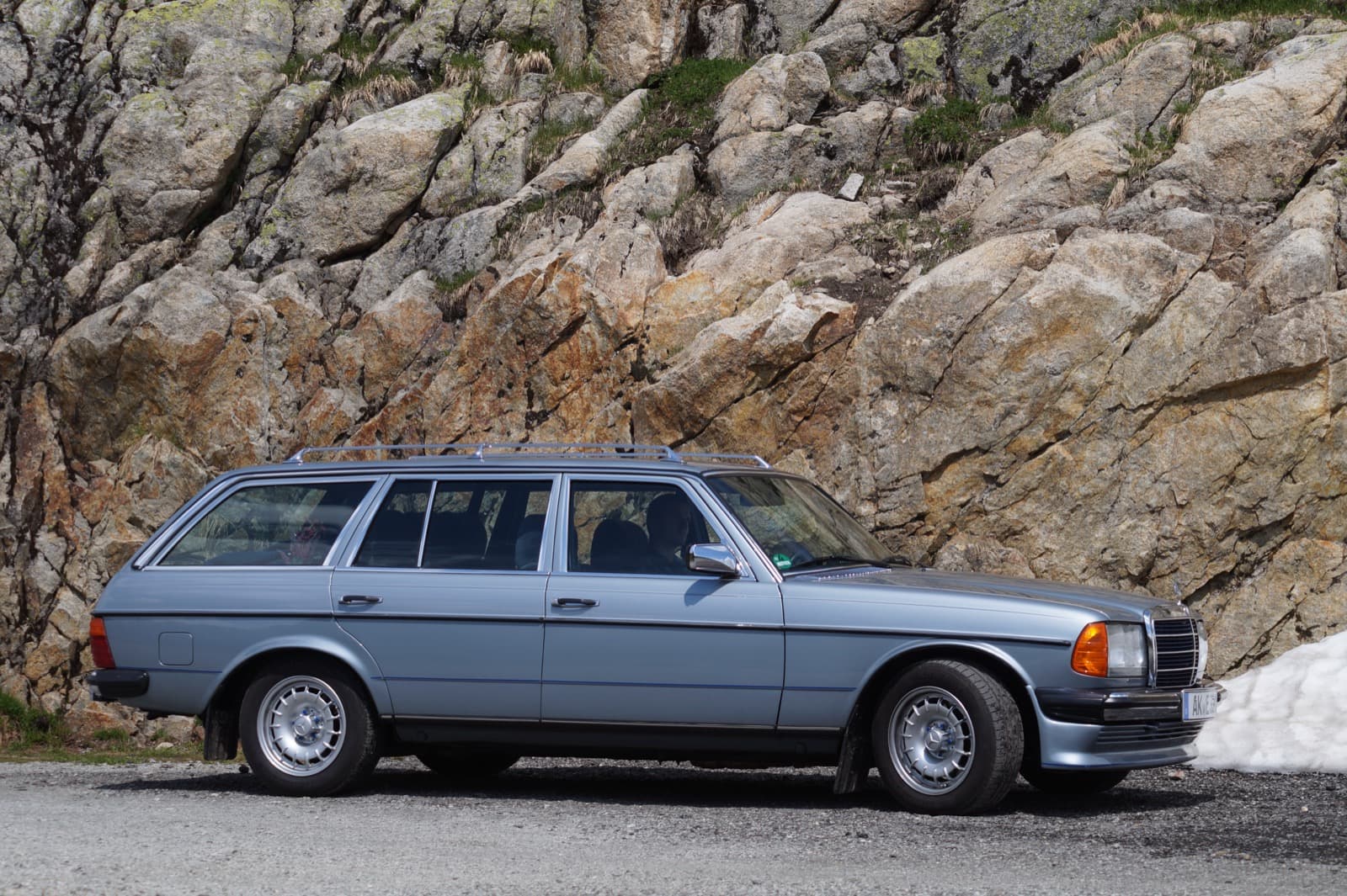 Hellblaues W123 T-Modell mit Dachreling im Profil vor einer Felswand