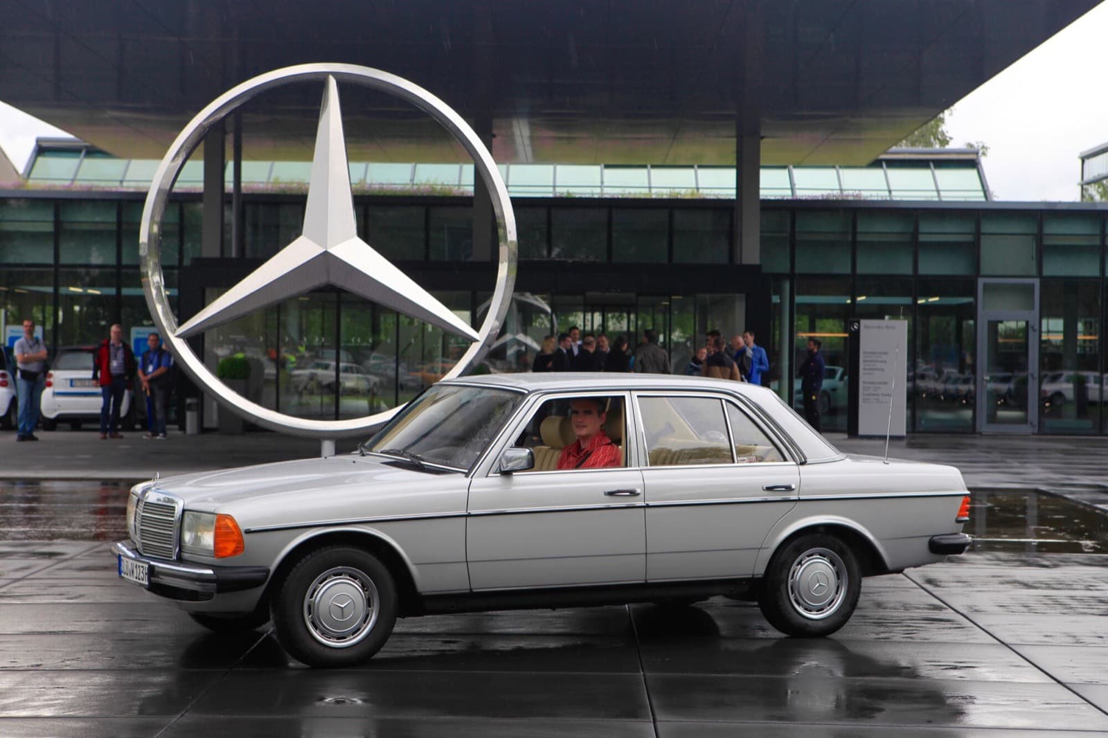 Silberne W123 Limousine im Profil vor einem großen Mercedes-Stern